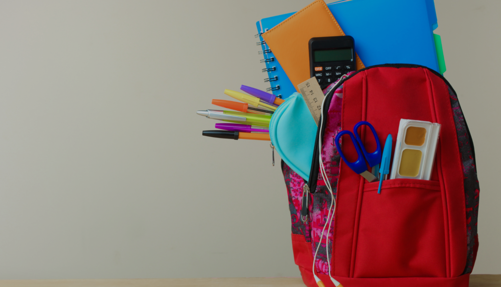 child's red backpack filled will school supplied like folders, pens pencils, note books and a calculator