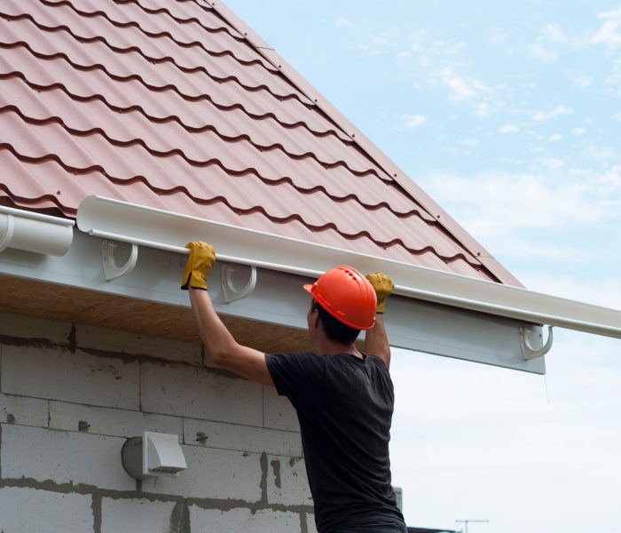 Photograph of construction worker installing gutter system on title roof.